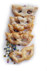 Italian sweet crisp pastry deep-fried and sprinkled with sugar in shape of Carnival mask isolated on white background. Chiacchere or crostoli, bugie, cenci with confetti and paper serpentine