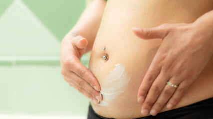 Fototapeta na wymiar Pregnant woman putting anti stretch mark cream on her belly to keep her skin hydrated and prevent scars. Woman using cream in the first months of pregnancy to prevent stretch marks during motherhood