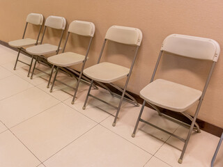A group of five white fold-able chair at a clean health clinic corridor.