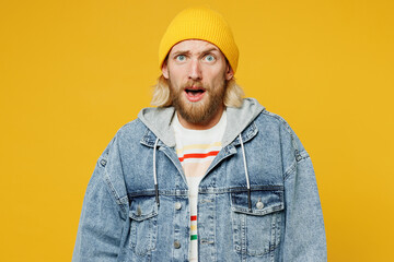 Young sad shocked panicked scared blond man he wears denim shirt hoody beanie hat casual clothes look camera with opened mouth isolated on plain yellow background studio portrait. Lifestyle concept.