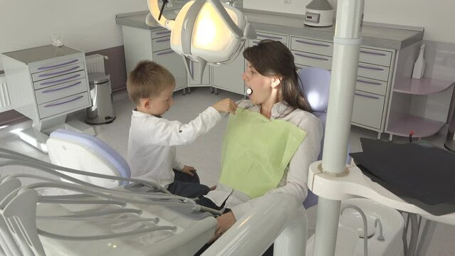 Young lady patient of little son playing as dentist