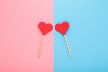Two red paper heart shapes on wooden sticks on light pink blue table background. Pastel color. Love...