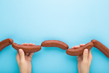 Young adult woman hands holding and showing string of raw fresh thick sausages for frying. Light blue table background. Pastel color. Closeup. Point of view shot. Top down view. - obrazy, fototapety, plakaty