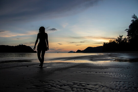 woman walking on the beach at sunset next to the sea and mountains