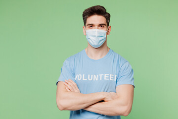 Young man wears protective disposable mask blue t-shirt white title volunteer hold hands crossed...