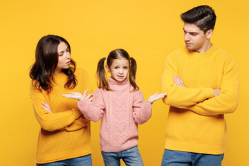 Young displeased dissatisfied parents mom dad with child kid girl 7-8 years old wear pink knitted sweater casual clothes spread hands say oops isolated on plain yellow background. Family day concept.