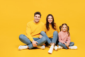 Full body young smiling happy cheerful parents mom dad with child kid girl 7-8 years old wear pink sweater casual clothes sitting look camera isolated on plain yellow background. Family day concept.