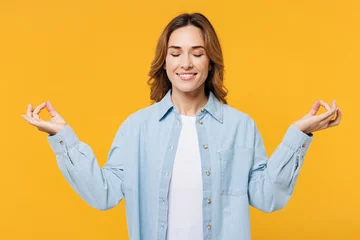 Poster Young woman she wear blue shirt white t-shirt casual clothes hold spreading hands in yoga om aum gesture relax meditate try to calm down isolated on plain yellow background studio. Lifestyle concept. © ViDi Studio