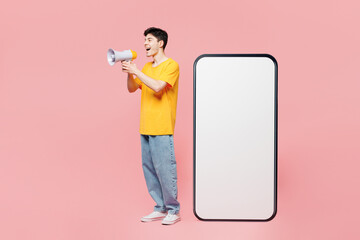 Full body young man in yellow t-shirt casual clothes big huge blank screen mobile cell phone smartphone with copy space mockup area scream in megaphone isolated on plain pastel light pink background