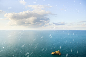 Blue sky with clouds and snowfall over sea.