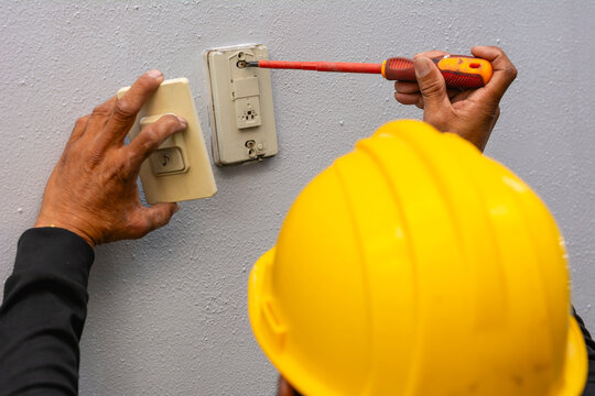 Close-up Of A Professional Electrician's Hand Installing Or Fixing A Wall Mounted Doorbell Push Button Switch With A Screwdriver.