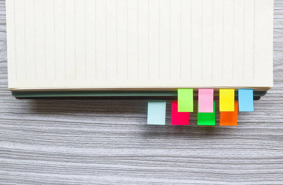 Colorful sticky notes among stack of books. Colorful sticky note bookmarks are attached to the notebook. Bookmarks in book on wooden table