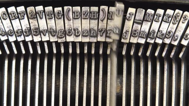 Old vintage mechanical typewriter typebars hammers striking the letters, close-up macro detail