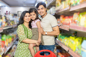 Portrait of Happy indian family of three shopping for groceries at the supermarket. mother holding little girl in her arm.