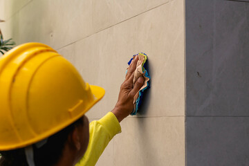 Over-the-shoulder view of a construction worker in a yellow hard hat meticulously cleaning a marble...
