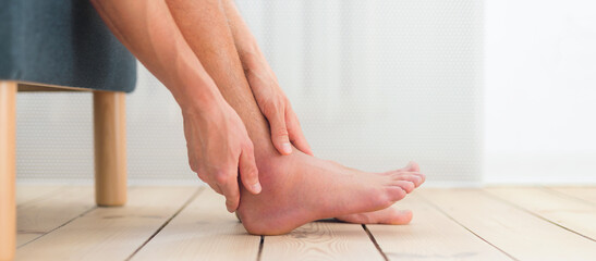 Ankle sprain. Man hold his sprained, swollen ankle sitting on the sofa at home.
