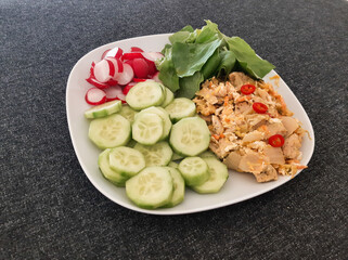 Homemade grilled chicken with rice and kimchi, green salad, cucumber and radish served on a white plate