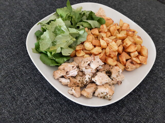 Homemade grilled chicken with french fries and green salad, served on a white plate