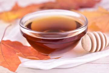 Maple syrup in a glass bowl against a background of maple leaves.Close-up.
