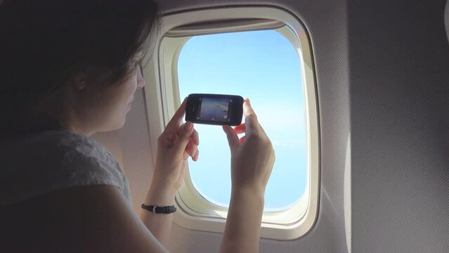 Pretty woman takes pictures with mobile phone on airplane window