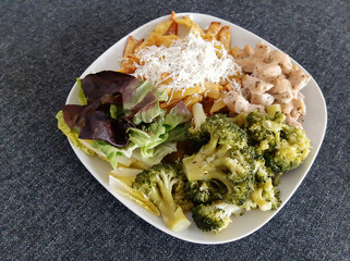 Homemade grilled chicken with french fries, broccoli, cheese and green salad, served on a white plate
