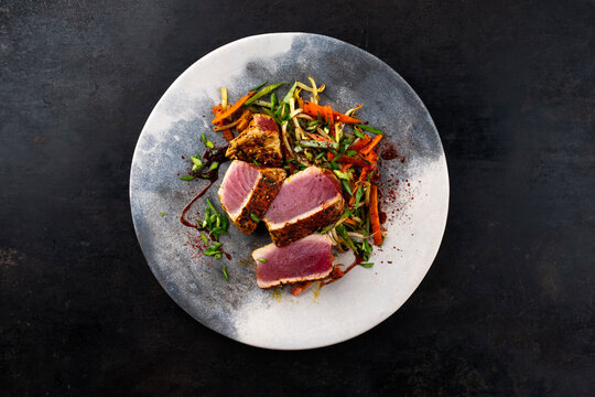 Traditional Japanese gourmet tuna fish steak tataki with vegetable slices and soy sprouts with sweet dour sauce served as top view on a Nordic design plate with copy space 