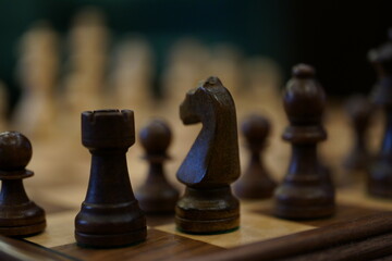 Black and white chess pieces arranged on a wooden table, juxtaposed against a wall