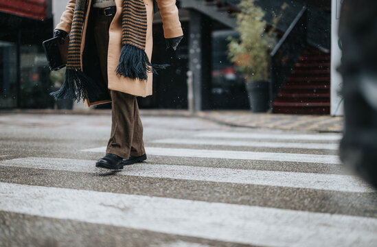 Close-up of a business person's lower body, crossing a snowy city street. Winter urban scene depicting solo pedestrian commute during snowfall.