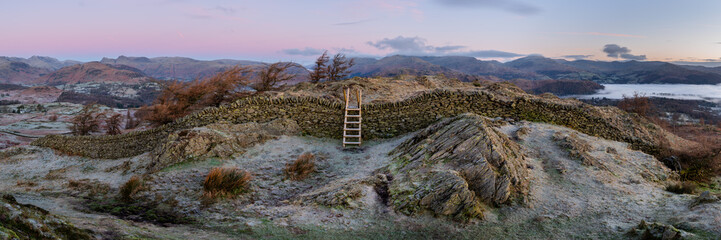 Lake District sunrise panorama seen from Black Crag with wooden stile over stone wall. Aerial views towards Windermere and Langdale. - 727851961