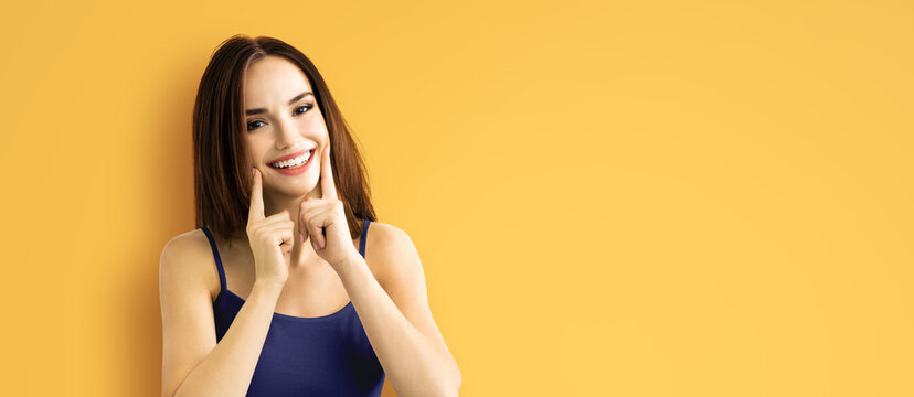 Portrait image - excited brunette woman showing pointing finger her tooth smile, in violet blue cloth, isolated yellow background. Optimistic, positive happy feeling or dental teeth care ad concept