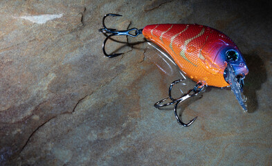 Wet red and orange fishing lure on a rock