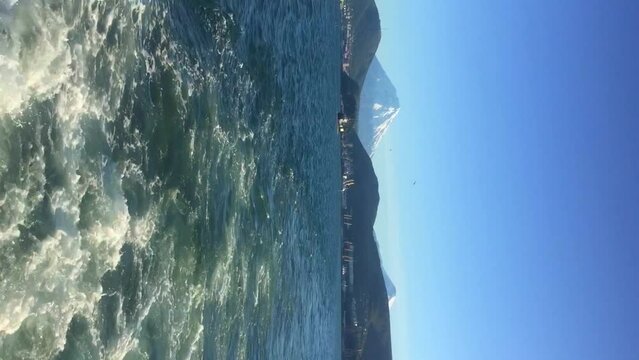 Rear view of Koryaksky volcano rising over Petropavlovsk-Kamchatsky city from boat sailing on Avacha bay ina sunny summer day. Real time handheld vertical video. Beauty in nature theme.