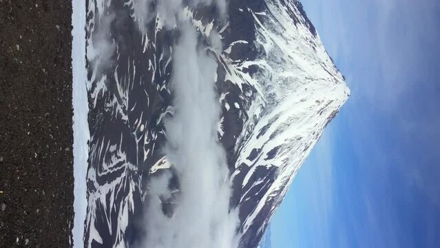 View from Avachinsky volcano slope of snowy Koryaksky volcano peak rising over clouds in a sunny morning in Kamchatka, Russia. Real time handheld video. Extreme travel theme.