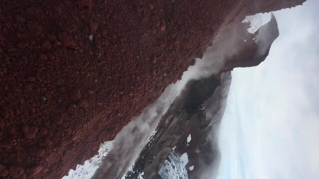 Side view of Avachincky volcano active crater with black lava cork covered with snow in Kamchatka, Russia. Koryaksky volcano peak rising over clouds in background. Real time handheld vertical video.