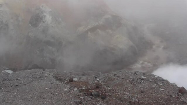 Mountain river of glacial water and acids flows in Mutnovsky volcano crater full of smoke, steam and fumes in Kamchatka, Russia. Real time handheld video. Volcanic activity theme.