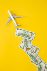 Airplane and dollar bills on a yellow background, top view. Creative composition, concept of income...