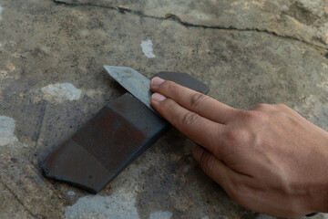 Knife sharpening on knife sharpening stone. Background of cement floor and hand holding knife...