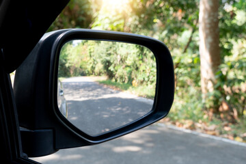 Rear view mirror of car on asphalt road background. Copy space and blurred of green forest at day...