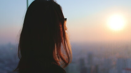 Woman enjoy cityscape sunset aerial view standing near the window. Close up long hair girl...