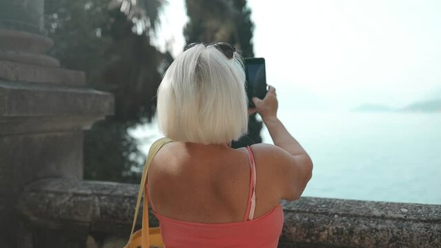 Travel adventure woman taking smart phone photograph on mountain lake enjoying beautiful nature landscape wanderlust. Como in Italy. High quality FullHD footage