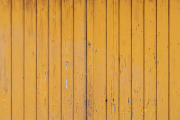 Old wooden texture with weathered yellow paint on the exterior wall. The surface is damaged and parts of the color are chipped. The hardwood facade can be a background.