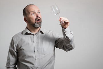 Surprised Caucasian man staring at empty wine glass, white background. Conceptual image of The Dry...