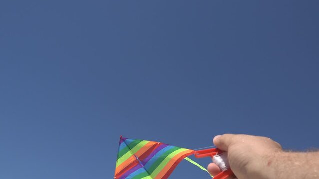 Hand holding colored kite flying in blue sky