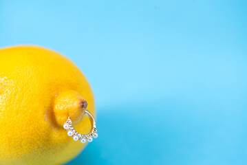 Intimate piercing. Minimal piercing concept. Lemon with piercing on blue background