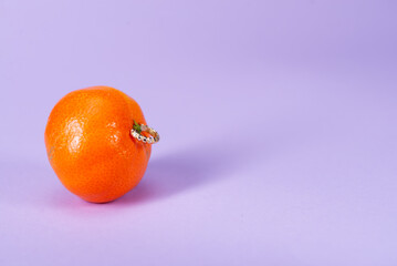Intimate piercing. Minimal piercing concept. Mandarin with piercing on lilac background