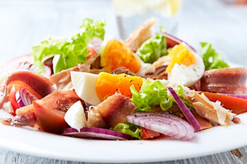 Salad with hard-boiled eggs, tomatoes, lettuce, red onion and smoked mackerel on bright wooden...