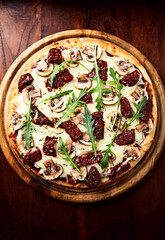 Pizza with mozzarella cheese, marinated tomatoes and fresh rocket. Dark wooden background. Top view.	