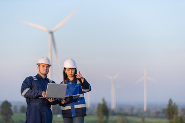 Two engineers working and holding the report at wind turbine farm Power Generator Station on mountain,Thailand people,Technician man and woman discuss about work