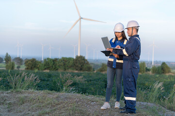 Two engineers working and holding the report at wind turbine farm Power Generator Station on mountain,Thailand people,Technician man and woman discuss about work