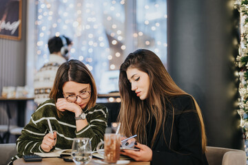 Intimate moment shared by two women in a cafe adorned with festive lights, evoking a warm, holiday atmosphere.